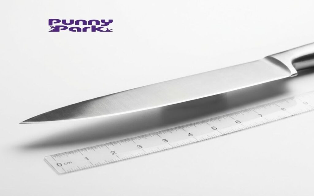 A sharp stainless steel chef's knife resting diagonally on a white surface. A clear ruler placed underneath shows the blade length approaching 8 or 9 inch.